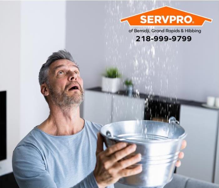 A person holds a bucket to catch water dripping from the ceiling.