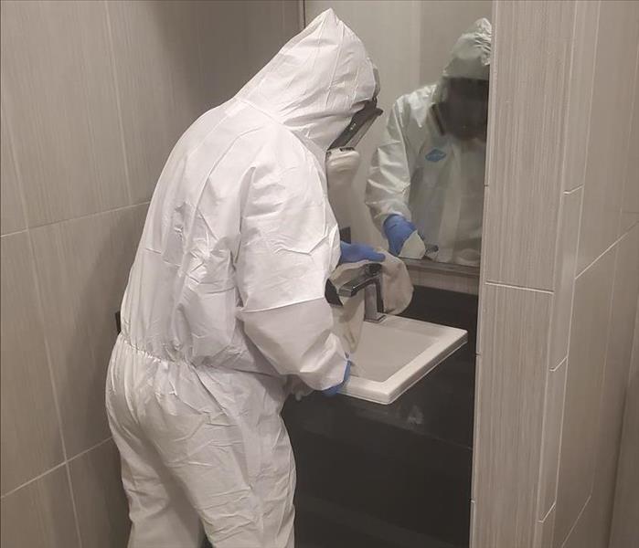 employee in full PPE wiping down the bathroom sink