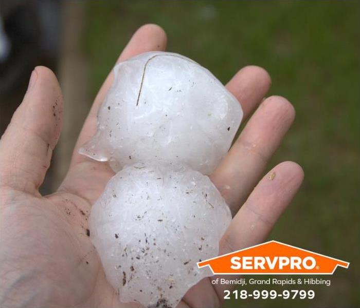 Two baseball-sized hailstones sit in the palm of a man’s hand.