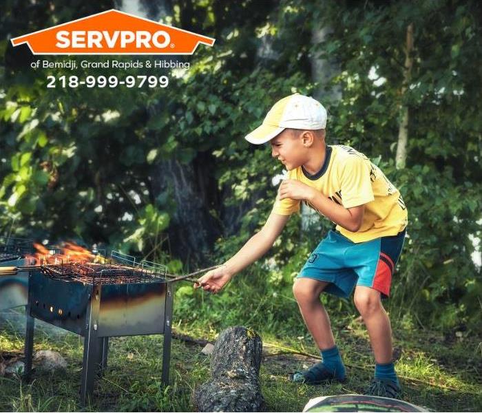 A curious child plays with the fire on an outdoor grill.